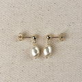 Simulated baroque pearl drop earrings with gold ball studs on linen