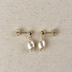 Simulated baroque pearl drop earrings with gold ball studs on linen
