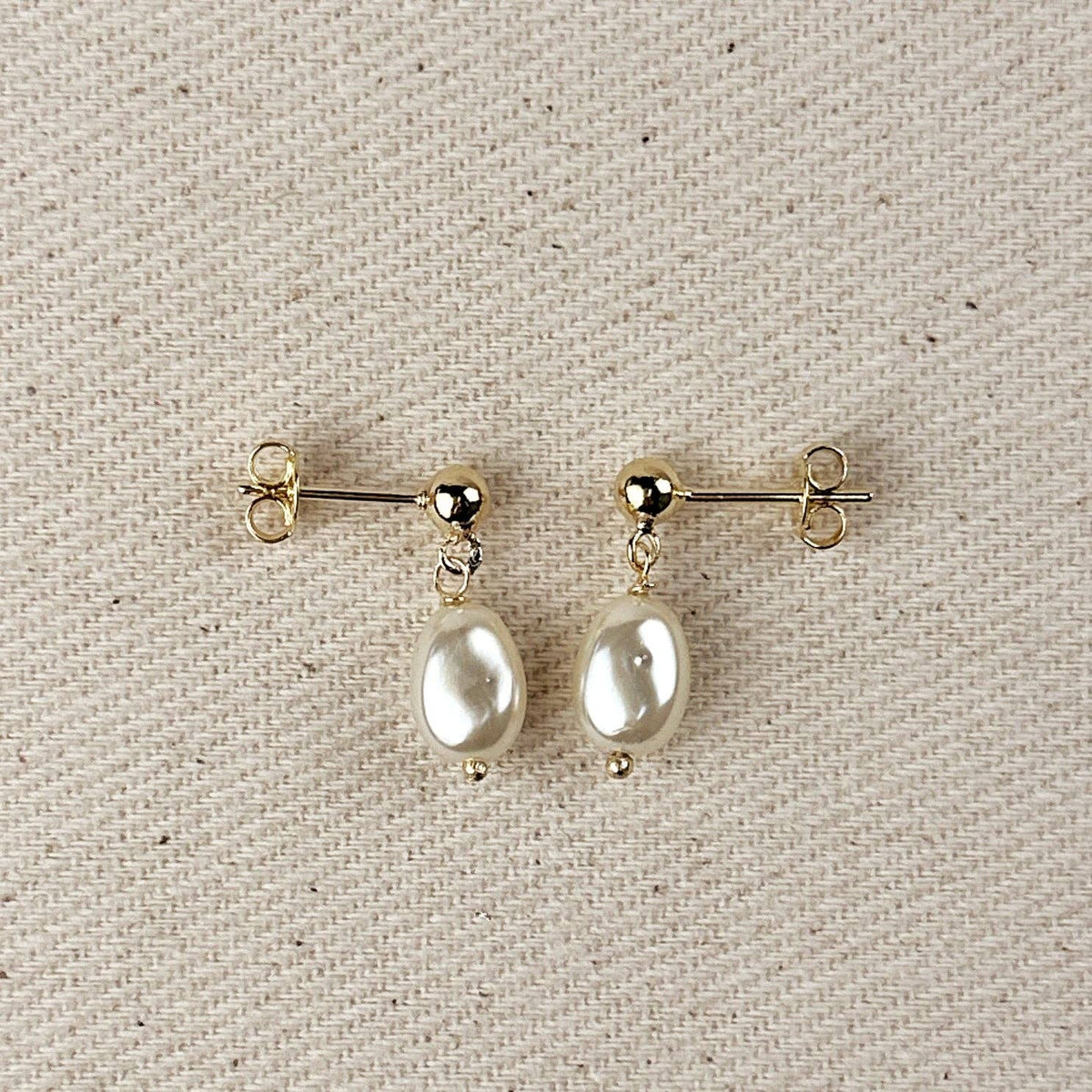 Simulated baroque pearl drop earrings with gold ball studs on linen