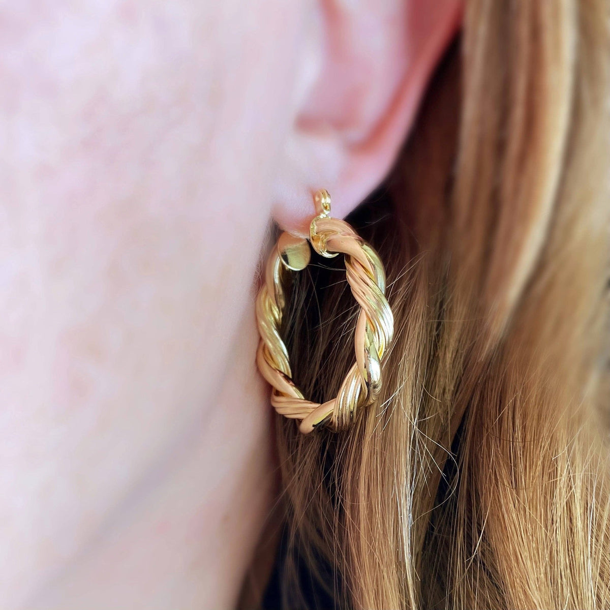 Twisted gold hoop earring worn on the ear
