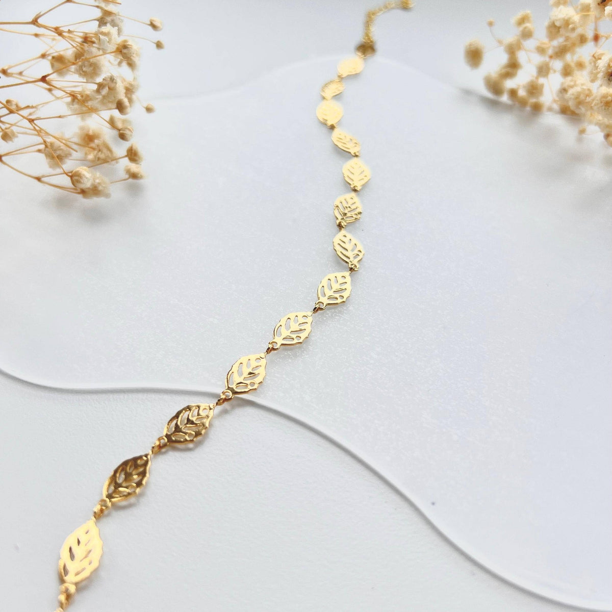 Gold leaf charm bracelet draped on a white surface