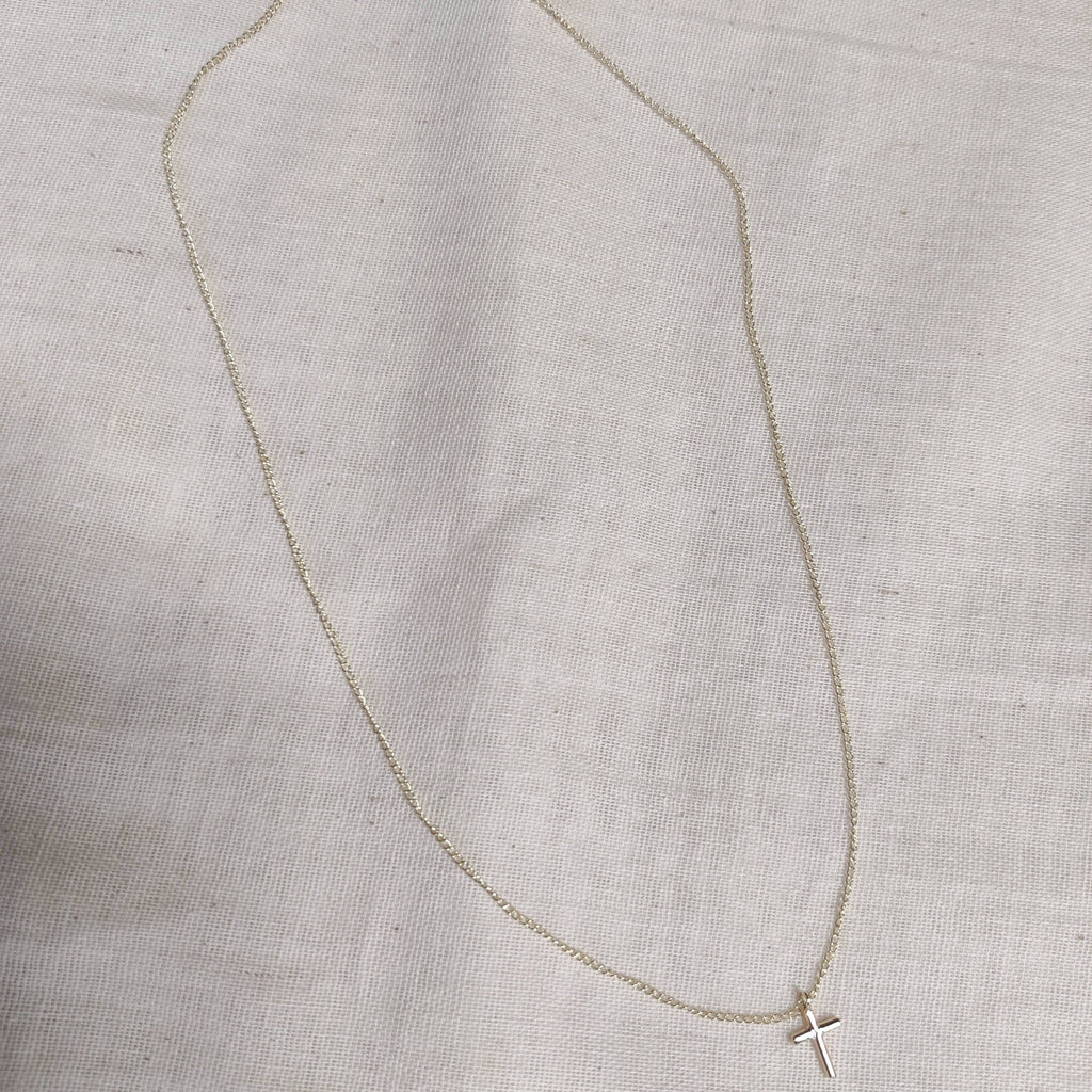 Petite cross necklace in 9ct white gold laid flat on linen