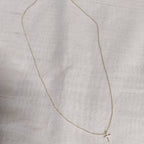 Petite cross necklace in 9ct white gold laid flat on linen