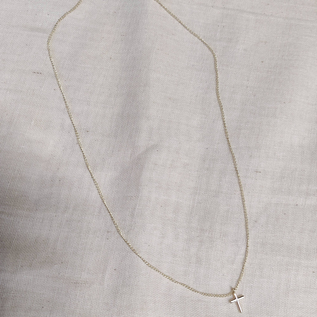 Petite cross necklace in 9ct white gold laid flat on linen