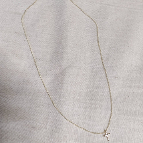 Petite cross necklace in 9ct white gold laid flat on linen